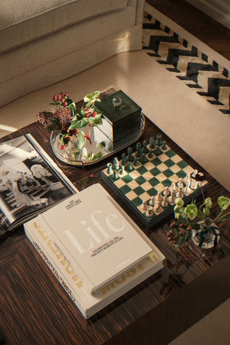 Coffee table styled with art books, a green chess set and a small posy